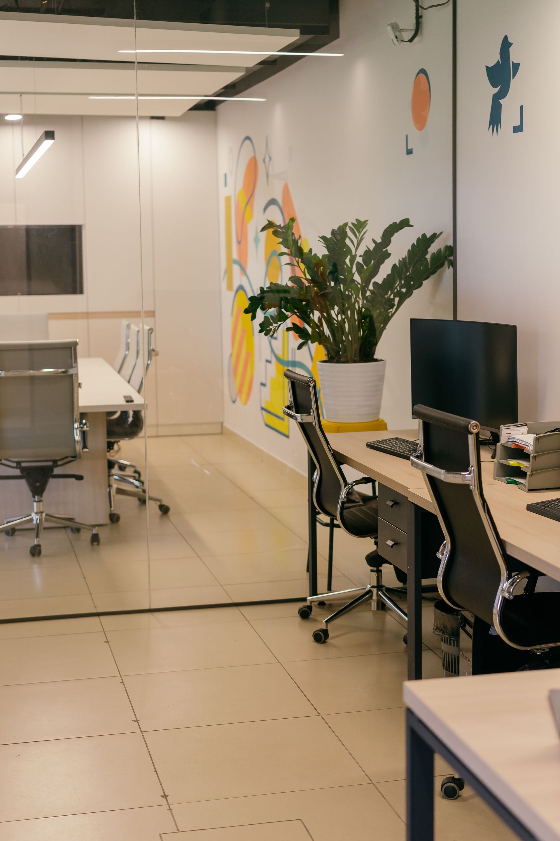 Spacious and contemporary office interior with glass partitions, stylish furniture, and vibrant wall art.