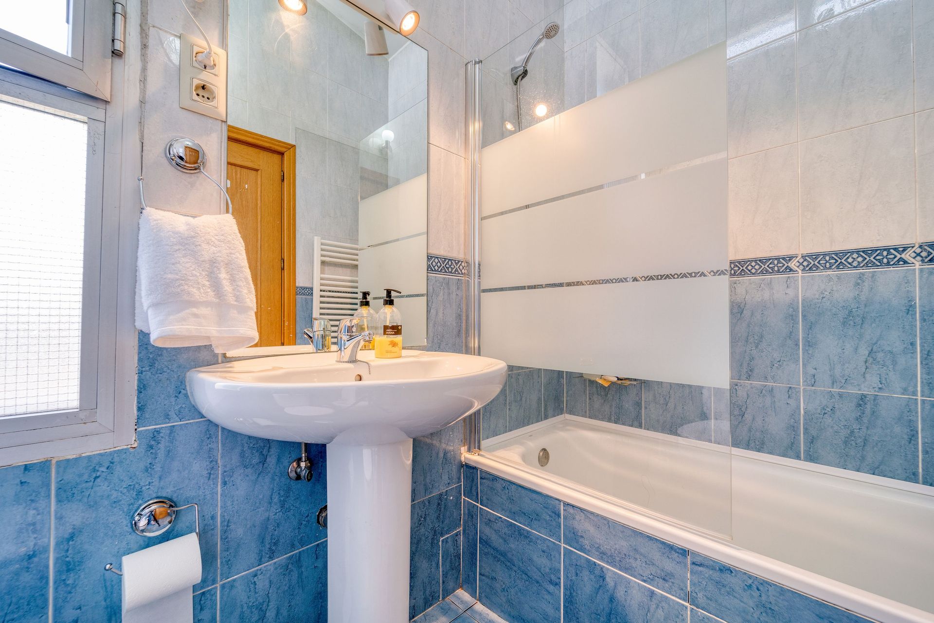 Bright minimalist bathroom with modern blue tiles, glass shower, and a clean white sink.